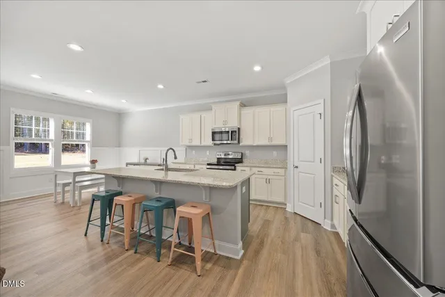 a kitchen with stainless steel appliances a refrigerator a stove a sink dishwasher and white cabinets with wooden floor