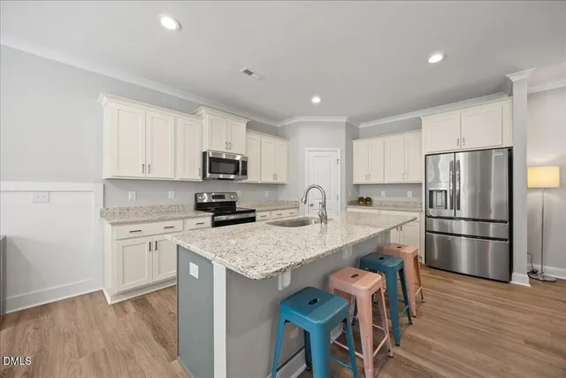 a kitchen with a refrigerator a stove a sink and white cabinets with wooden floor