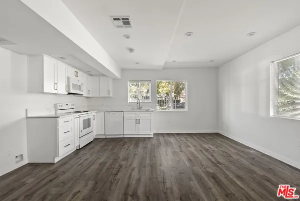 a kitchen with white cabinets a wooden floor and a window