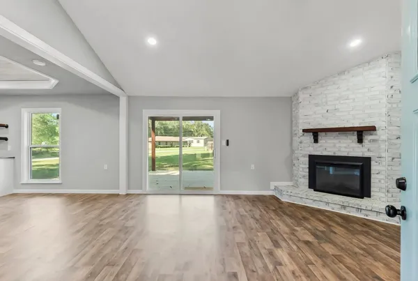 a view of an empty room with wooden floor fireplace and a window