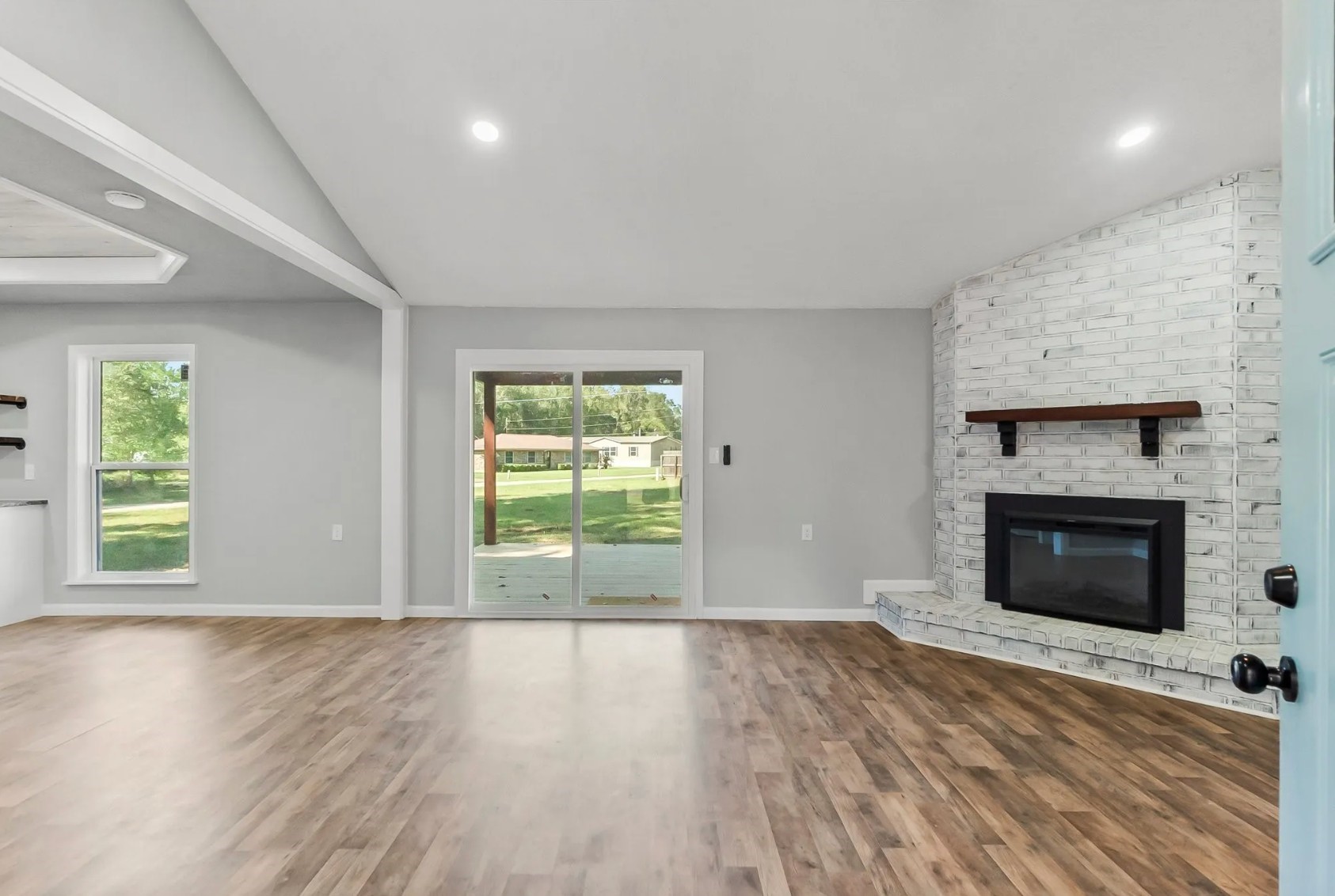 749 County Road 774 Buna, TX 77612 - Photo 4 of 9 Discover a bright and inviting living room featuring elegant hardwood-looking floors, a charming white brick fireplace, and expansive glass doors that seamlessly connect you to the outdoors.