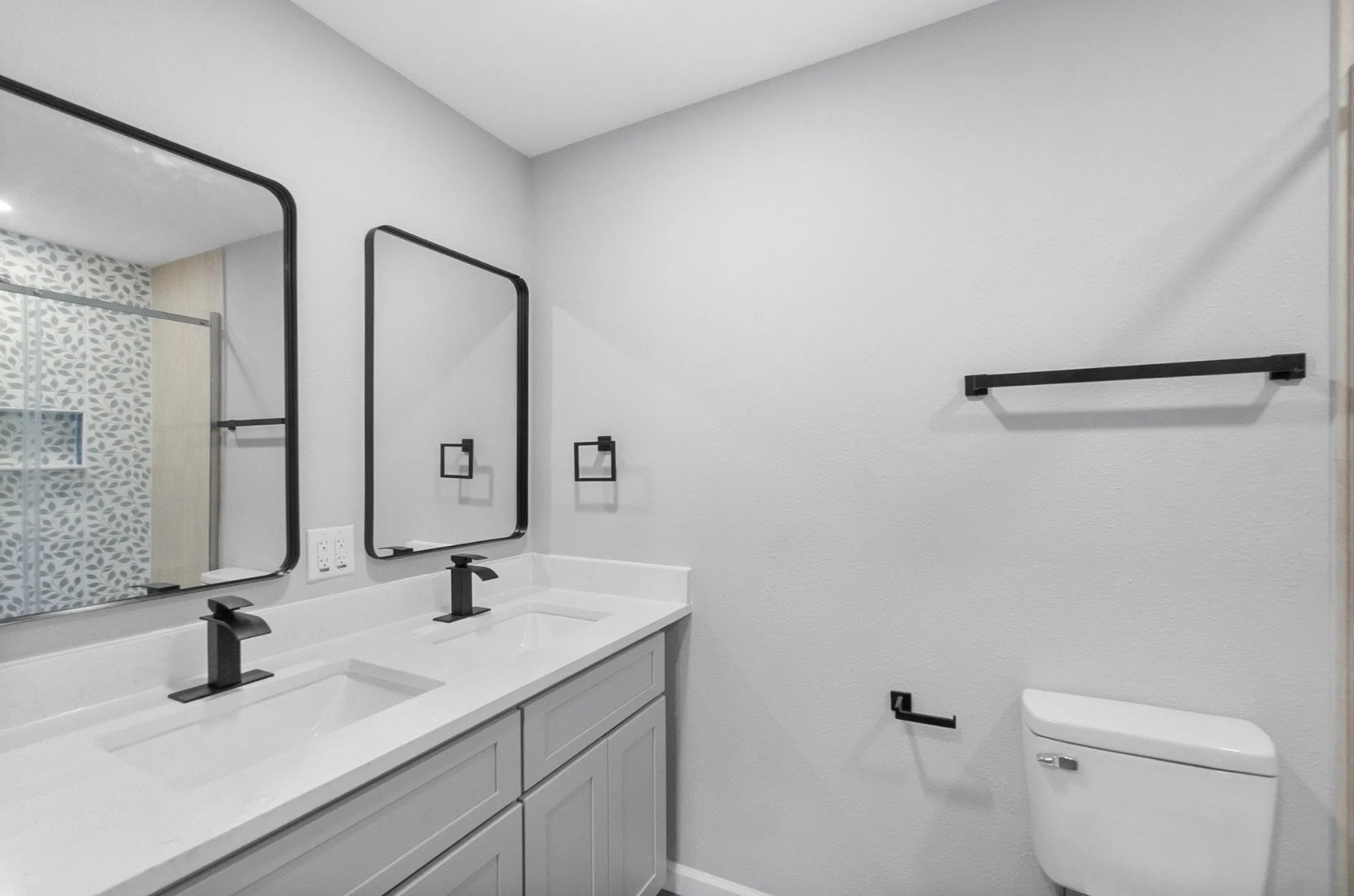 749 County Road 774 Buna, TX 77612 - Photo 7 of 9 This modern bathroom offers a sleek double vanity with elegant black fixtures, complemented by a stylishly patterned shower wall, perfect for a touch of luxury in your daily routine.