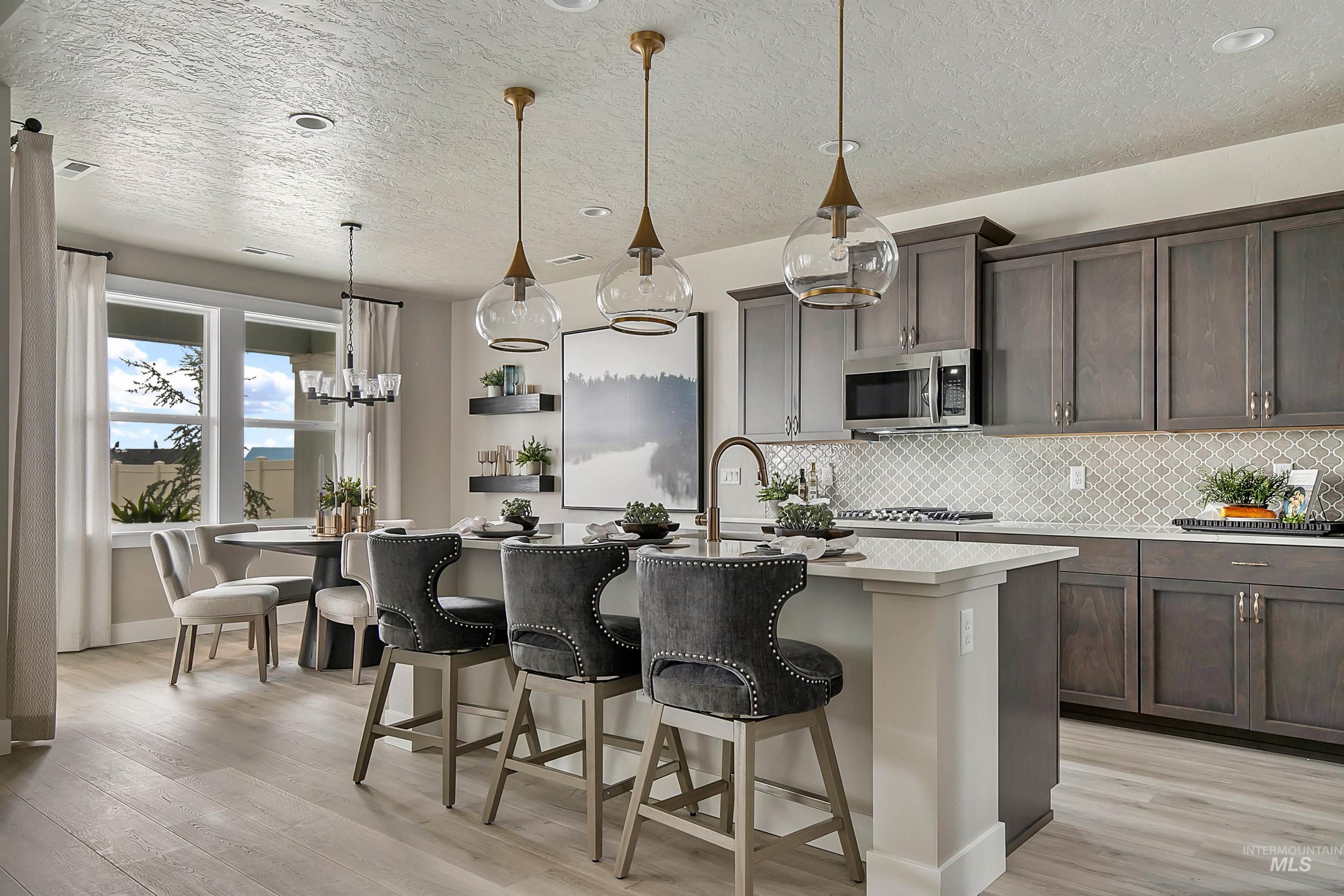 5877 West Ladle Rapids Street Meridian, ID 83646 - Photo 4 of 11 Kitchen featuring decorative backsplash, hanging light fixtures, a breakfast bar, light wood-type flooring, and a textured ceiling