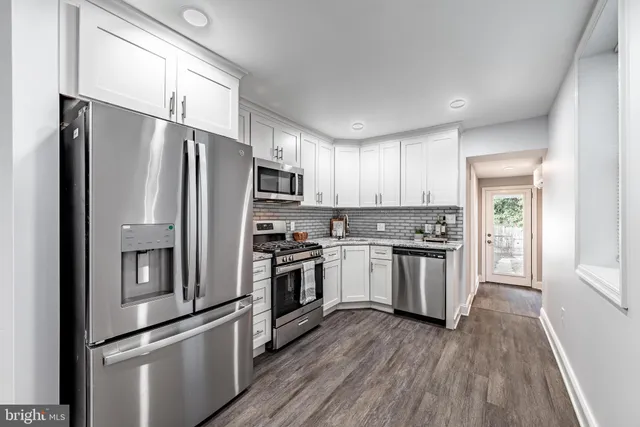 a kitchen with a refrigerator stainless steel appliances wooden floor and window