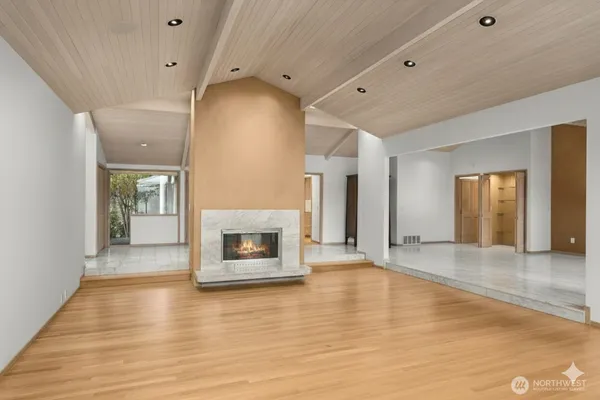 an empty room with wooden floor fire place and windows