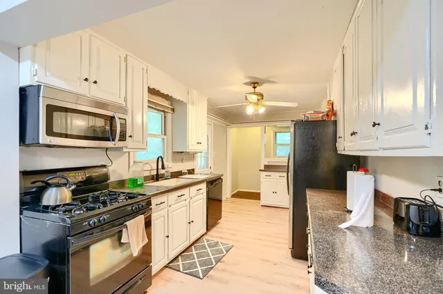 a kitchen with stainless steel appliances granite countertop a stove top oven a sink dishwasher and a refrigerator with wooden floor