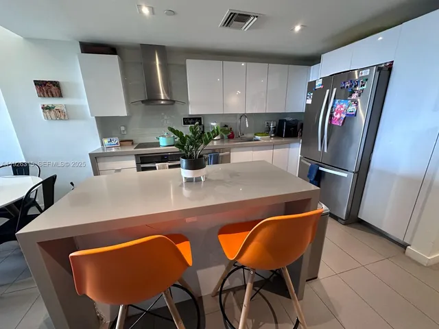 a view of kitchen with stainless steel appliances granite countertop dining table chairs and a refrigerator