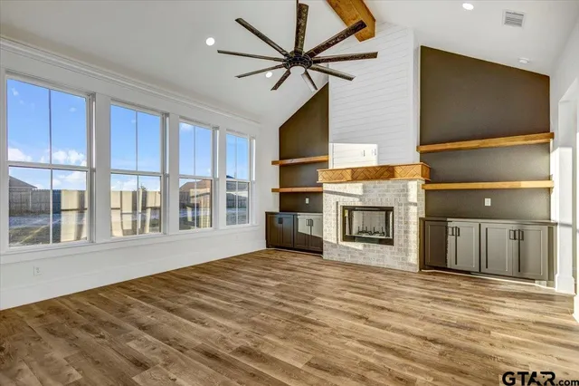 a view of a livingroom with a fireplace a ceiling fan and windows