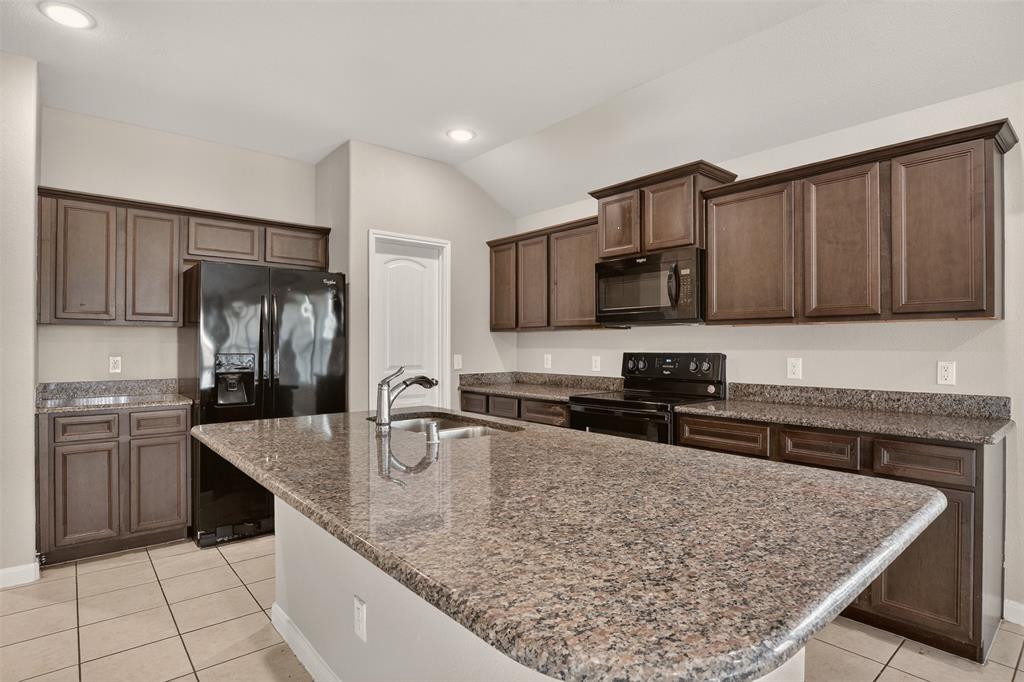 9105 Switchgrass Lane Forney, TX 75126 - Photo 15 of 20 Kitchen featuring an oversized island with an undermount sink, granite countertops, and dark wood-finish cabinetry