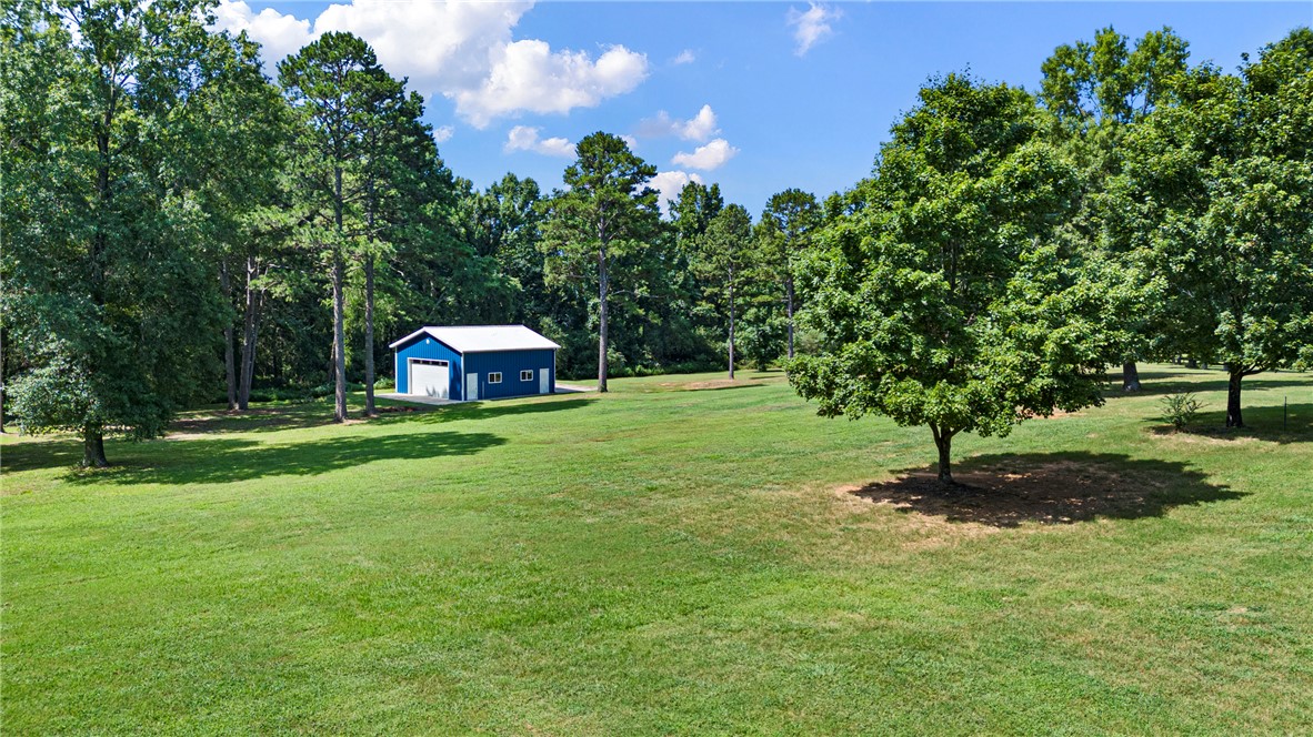 751 Walthall Road Russellville, AR 72802 - Photo 56 of 60 Blue metal outbuilding featuring a white garage door and white trim, surrounded by a large grassy area with mature trees