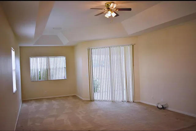 an empty room with a chandelier fan and windows