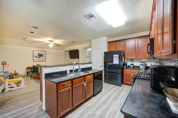a kitchen with stainless steel appliances granite countertop wooden cabinets a sink dishwasher a stove and a refrigerator with wooden floor