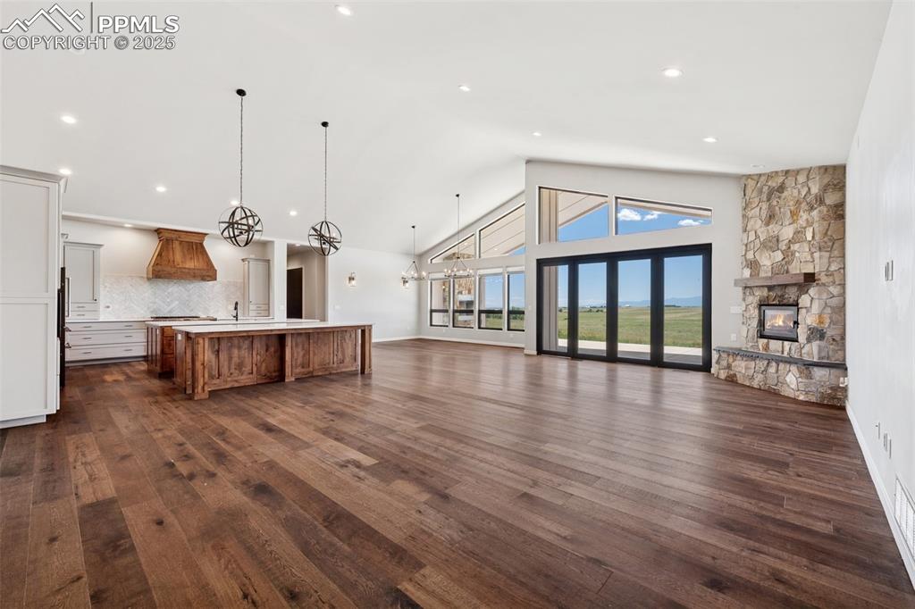 24365 Murphy Road Calhan, CO 80808 - Photo 7 of 48 Unfurnished living room with a stone fireplace, dark wood finished floors, high vaulted ceiling, recessed lighting, and a chandelier