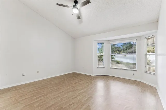 an empty room with wooden floor fan and windows