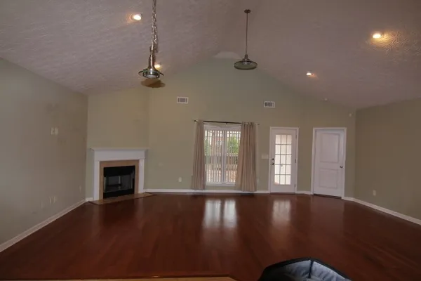 an empty room with wooden floor fireplace and windows