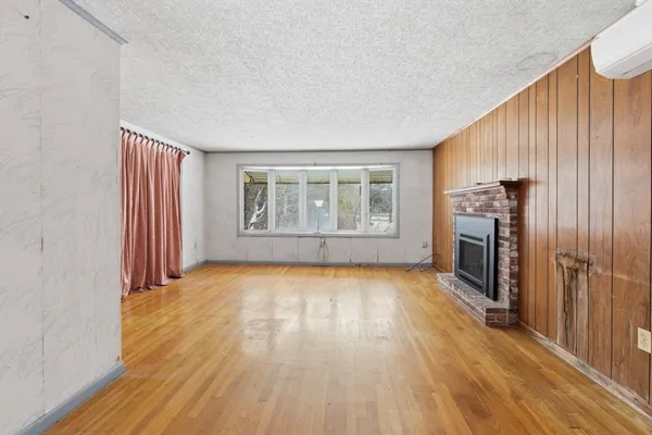 an empty room with wooden floor fireplace and windows