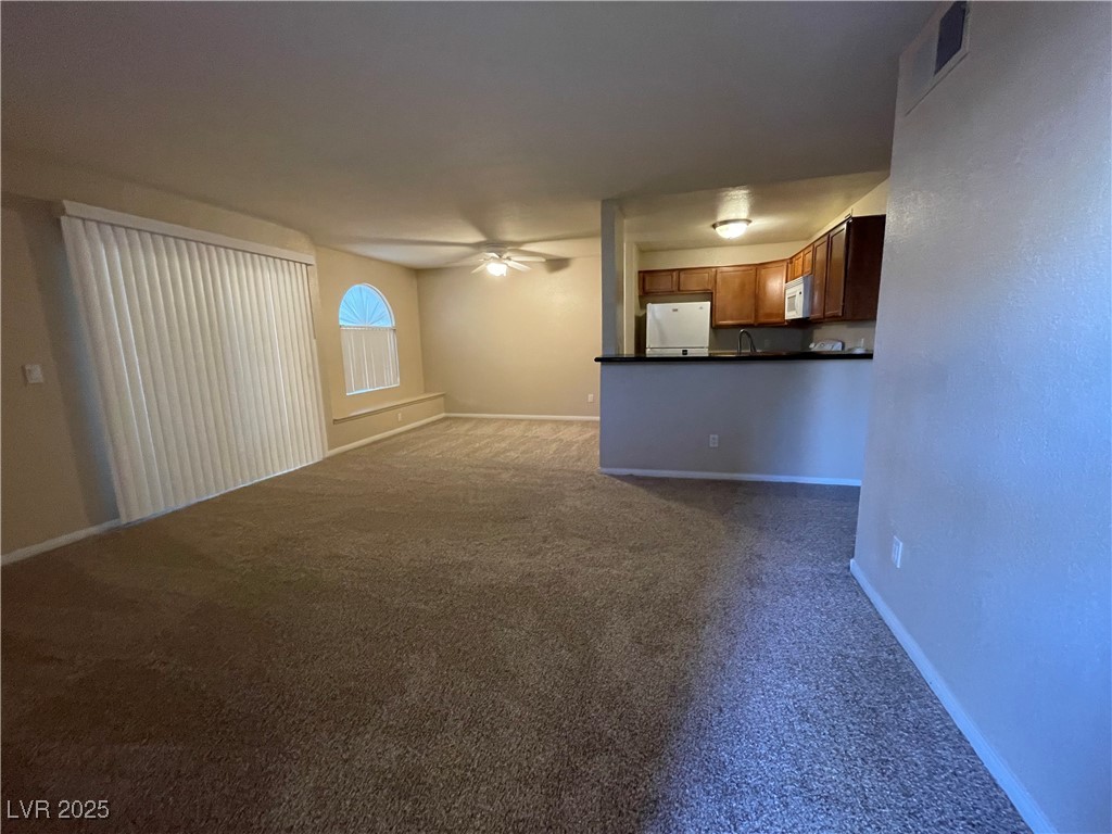 Unfurnished living room featuring dark carpet and a ceiling fan