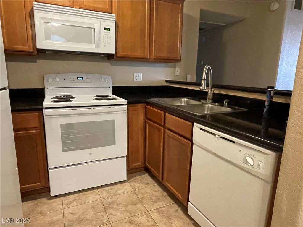 9325 West Desert Inn Road, Unit 149 Las Vegas, NV 89117 - Photo 4 of 20 Kitchen featuring white appliances, dark countertops, brown cabinetry, and light tile patterned floors