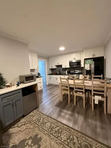 a kitchen with stainless steel appliances granite countertop a stove top oven a sink a dining table and chairs with wooden floor