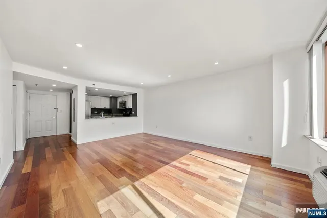 a view of empty room with kitchen view and wooden floor