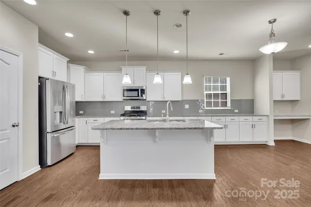 a kitchen with stainless steel appliances granite countertop a sink a stove a refrigerator and island with wooden floor