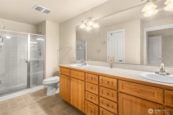 a bathroom with double vanity sink a toilet a shower and a large mirror