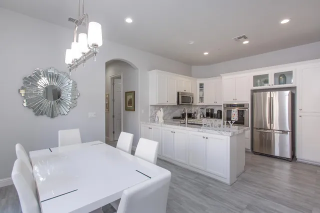 a kitchen with stainless steel appliances kitchen island granite countertop a refrigerator a sink dishwasher a dining table and chairs with wooden floor