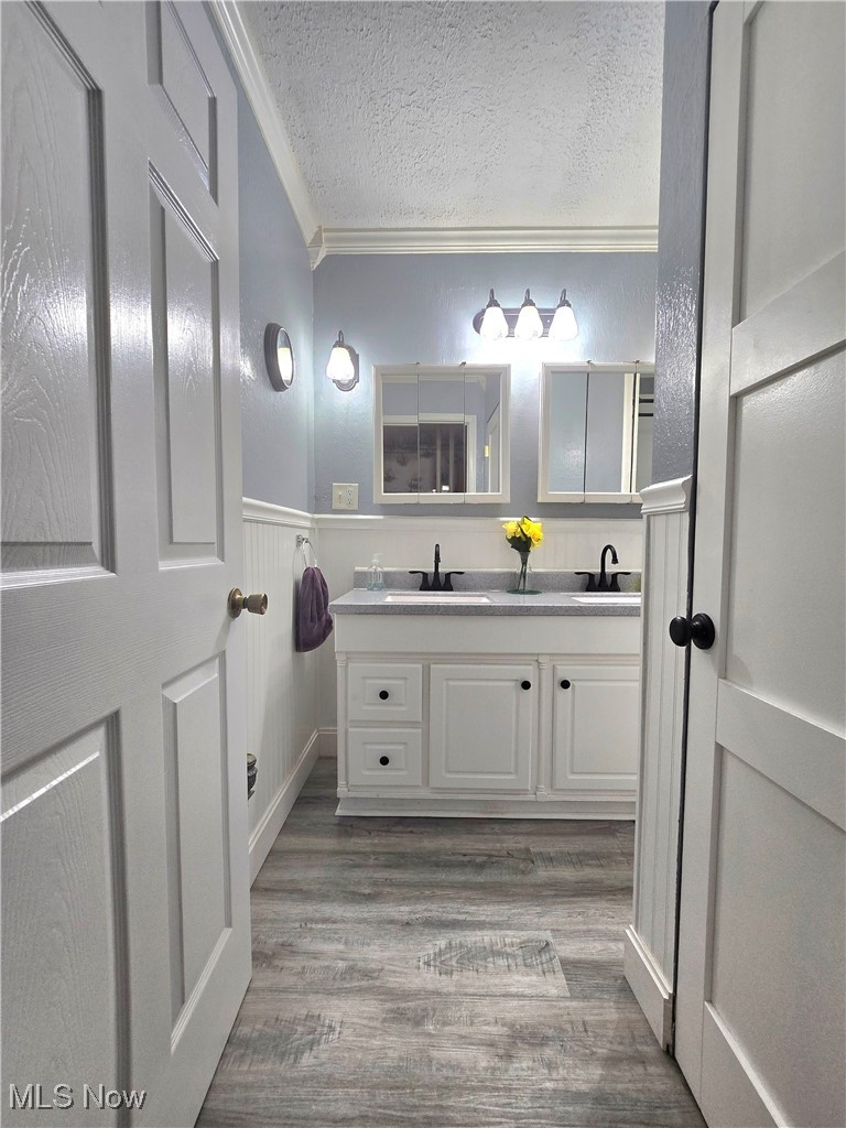 8019 Kroft Road Mount Perry, OH 43760 - Photo 34 of 41 Bathroom with double vanity, ornamental molding, light wood-style flooring, a textured ceiling, and wainscoting