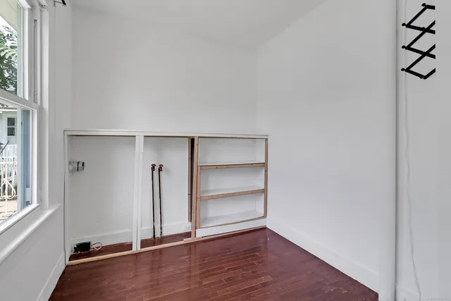 an empty room with wooden floor closet and windows