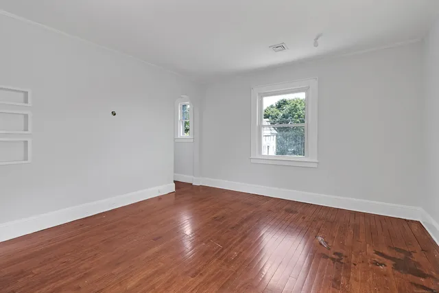 a view of an empty room with wooden floor and a window