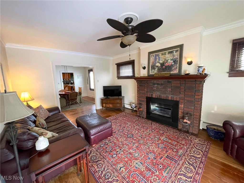 1302 Waverly Road Sandusky, OH 44870 - Photo 11 of 13 Living room featuring crown molding, wood-type flooring, a brick fireplace, baseboard heating, and ceiling fan