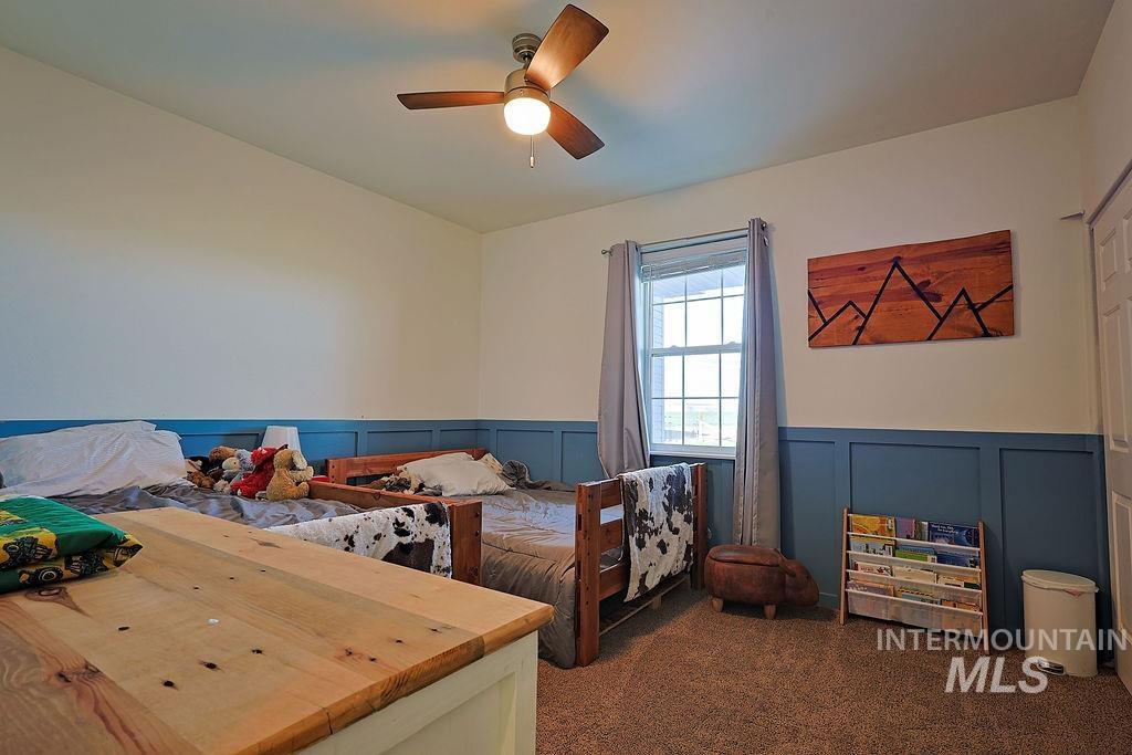 24 Harris Circle Shoshone, ID 83352 - Photo 19 of 39 Bedroom with a decorative wall, a ceiling fan, a wainscoted wall, and dark colored carpet