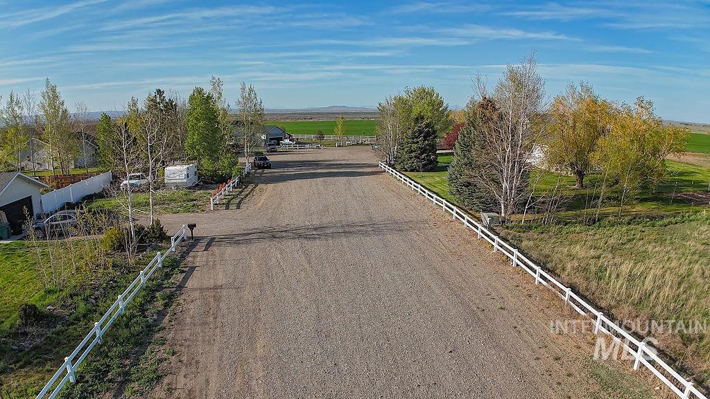 24 Harris Circle Shoshone, ID 83352 - Photo 32 of 39 Gravel driveway featuring white fencing along both sides, bordered by mature trees and green landscaping