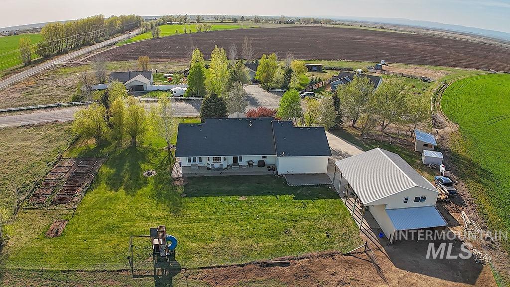 24 Harris Circle Shoshone, ID 83352 - Photo 36 of 39 Expansive rural property featuring a main residence with a rear deck, a large detached outbuilding with covered parking, a dedicated garden area, and mature trees
