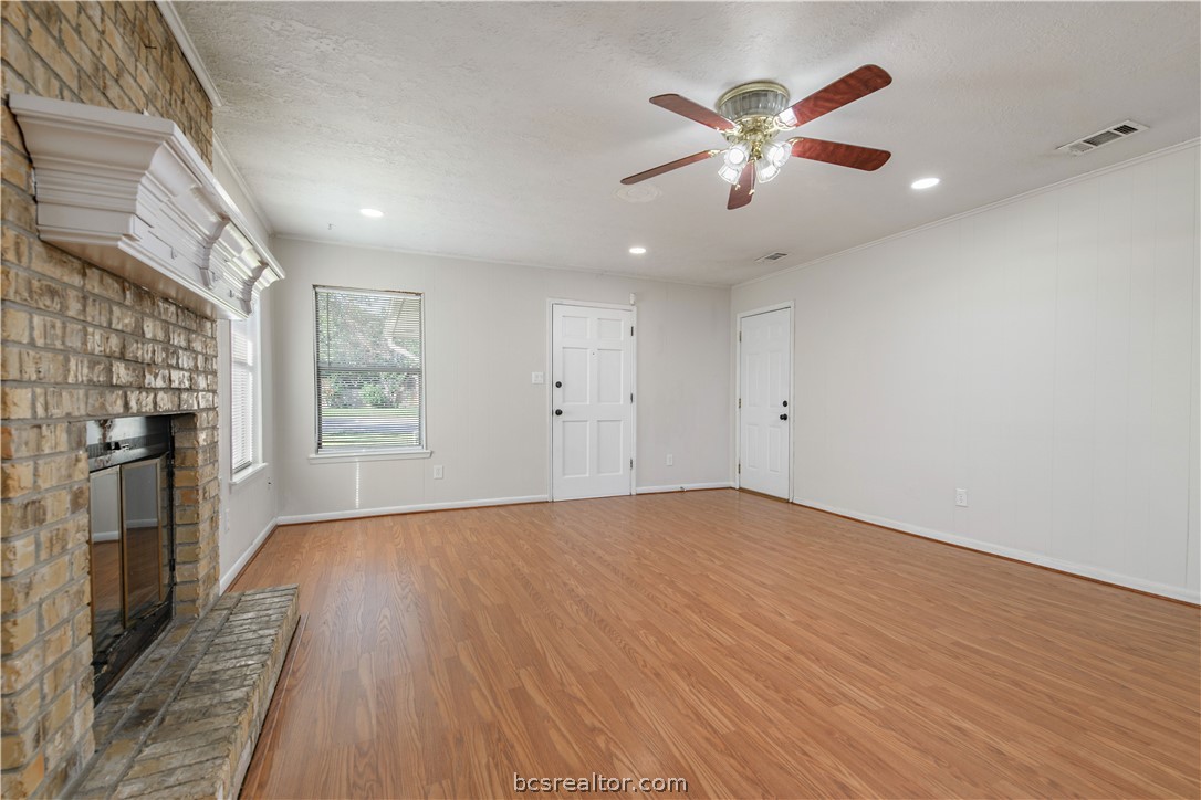 4403 Robinhood Circle Bryan, TX 77803 - Photo 5 of 19 an empty room with wooden floor a ceiling fan and fireplace