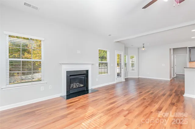 a view of an empty room with wooden floor fireplace and a window