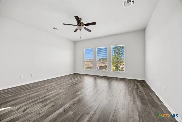 an empty room with wooden floor fan and windows