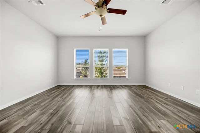an empty room with wooden floor chandelier fan and windows