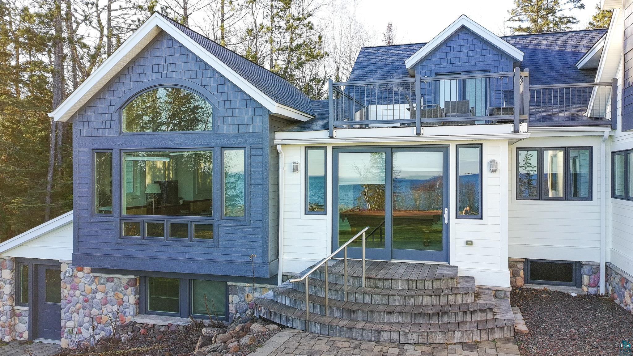 5163 Greenwood Road Duluth, MN 55804 - Photo 45 of 47 Multi-level exterior featuring white siding and blue shingle accents, a stone foundation, a second-story balcony, and large windows with transom details