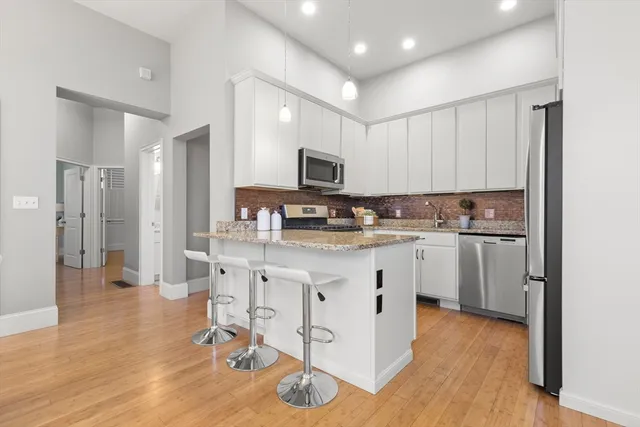 a kitchen with stainless steel appliances kitchen island granite countertop a stove a sink a refrigerator and white cabinets with wooden floor