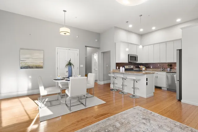 a kitchen with stainless steel appliances kitchen island granite countertop a stove a sink a refrigerator and white cabinets with wooden floor