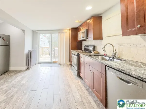 a kitchen with stainless steel appliances granite countertop a stove a sink dishwasher and white cabinets with wooden floor