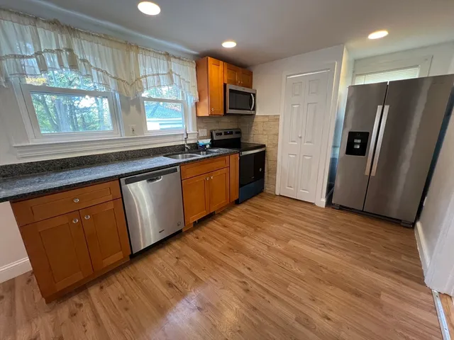 a kitchen with stainless steel appliances granite countertop a refrigerator a sink dishwasher a stove and white countertops with wooden floor