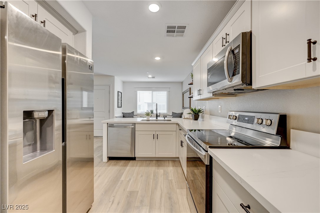 12106 Azure Gate Road, Unit 3 Las Vegas, NV 89183 - Photo 25 of 77 Kitchen featuring appliances with stainless steel finishes, white cabinetry, a peninsula, recessed lighting, and light wood-style floors