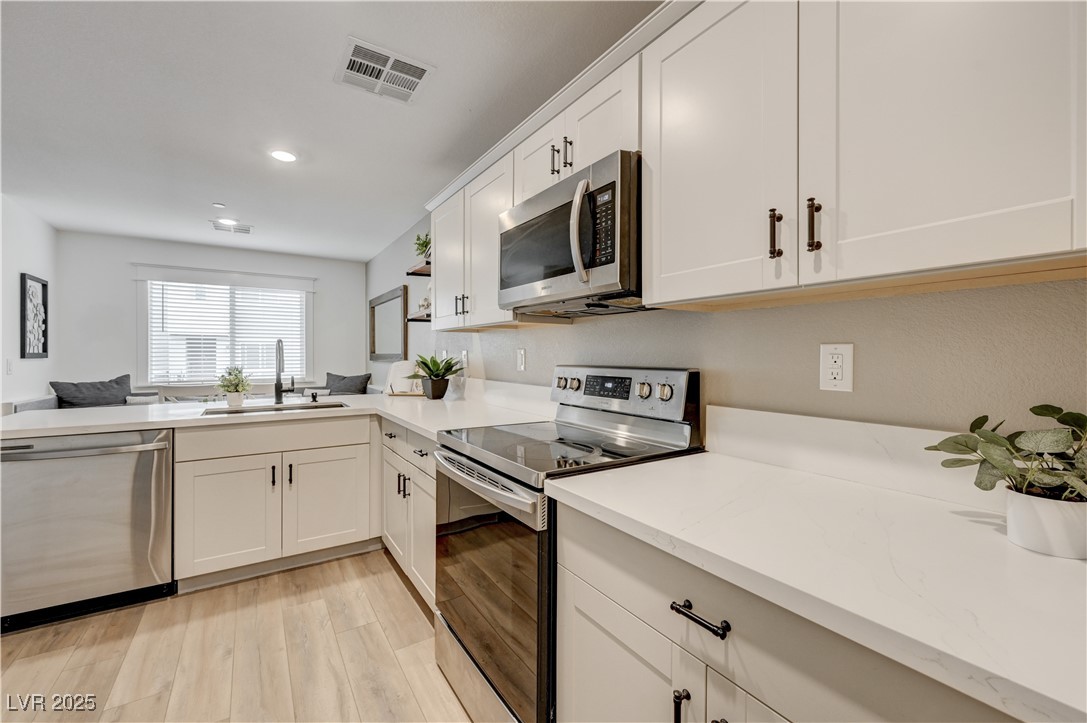 12106 Azure Gate Road, Unit 3 Las Vegas, NV 89183 - Photo 26 of 77 Kitchen featuring stainless steel appliances, white cabinetry, light wood-style floors, recessed lighting, and a peninsula