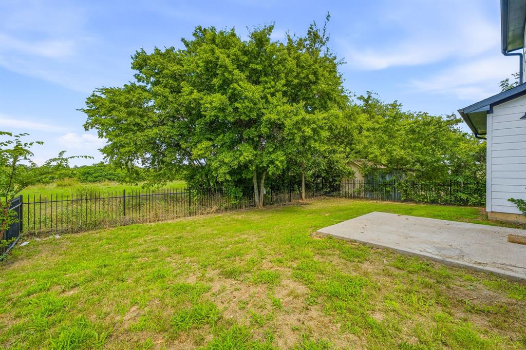 745 North Miller Avenue Stephenville, TX 76401 - Photo 31 of 31 Expansive backyard featuring a large tree, green lawn, concrete patio, and black metal fencing