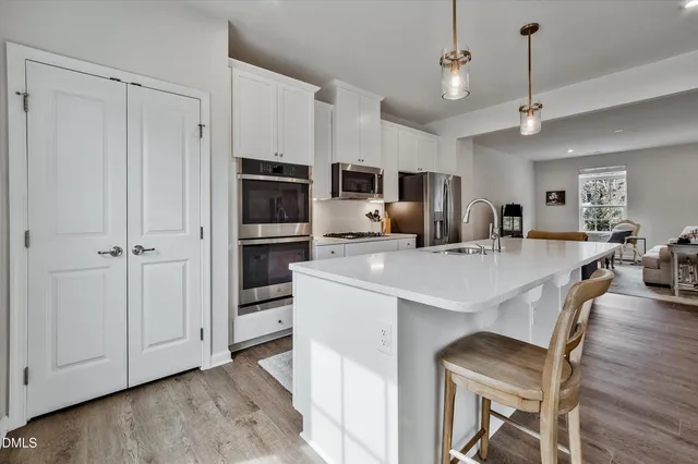 a large kitchen with kitchen island a large island in center island stainless steel appliances wooden floor and living room view