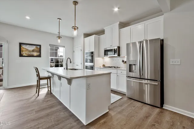 a kitchen with kitchen island a sink a refrigerator a stove and white cabinets with wooden floor