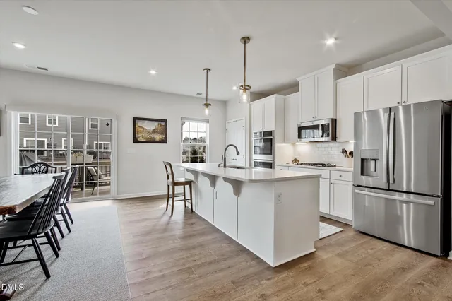 a kitchen with stainless steel appliances a refrigerator a stove a sink a dining table and chairs