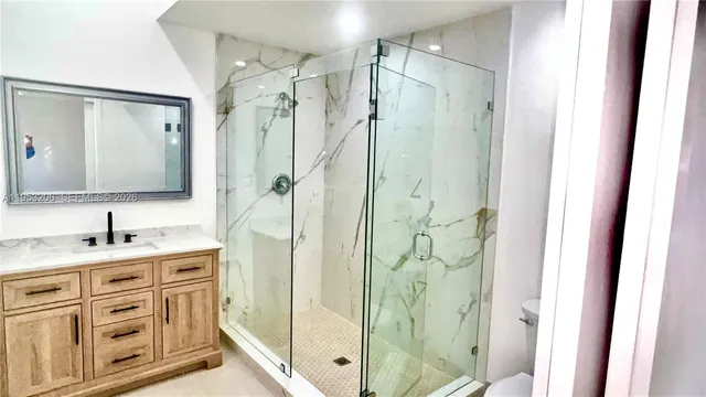 a bathroom with a granite countertop sink a mirror a glass door a shower and vanity